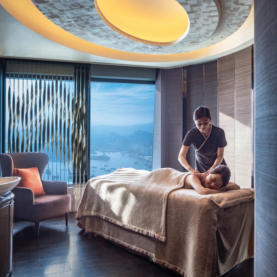 A masseuse gives a woman a shoulder massage in a spacious treatment room that looks out over the Hong Kong harbour at The Ritz-Carlton Spa.