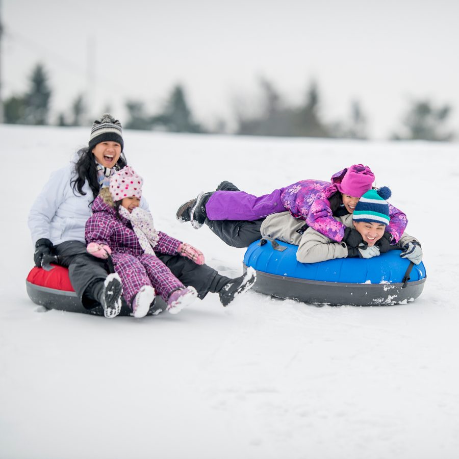 Adults and children toboggan on a snowy hill. 