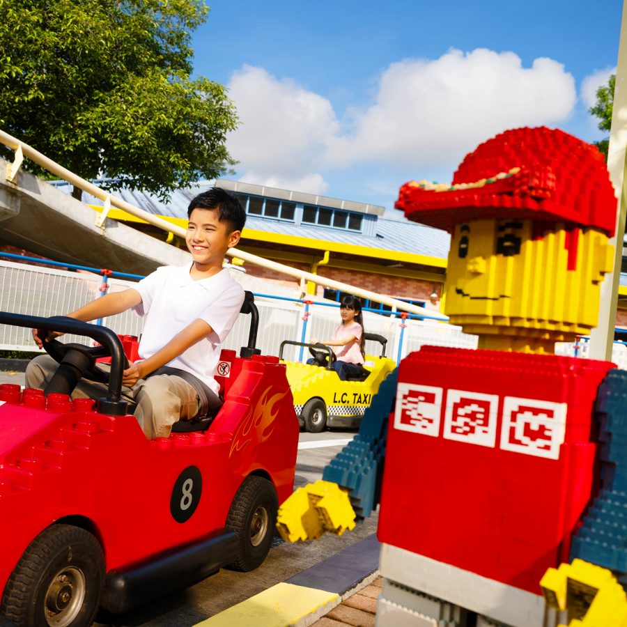 Children driving electric cars next to life-sized figures at the LEGO City Driving School in LEGOLAND Malaysia.
