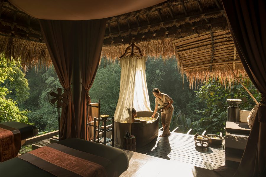 A female staff member placing flowers in a tub where a woman is soaking at the spa of Four Seasons Tented Camp Golden Triangle, Chiang Rai. 