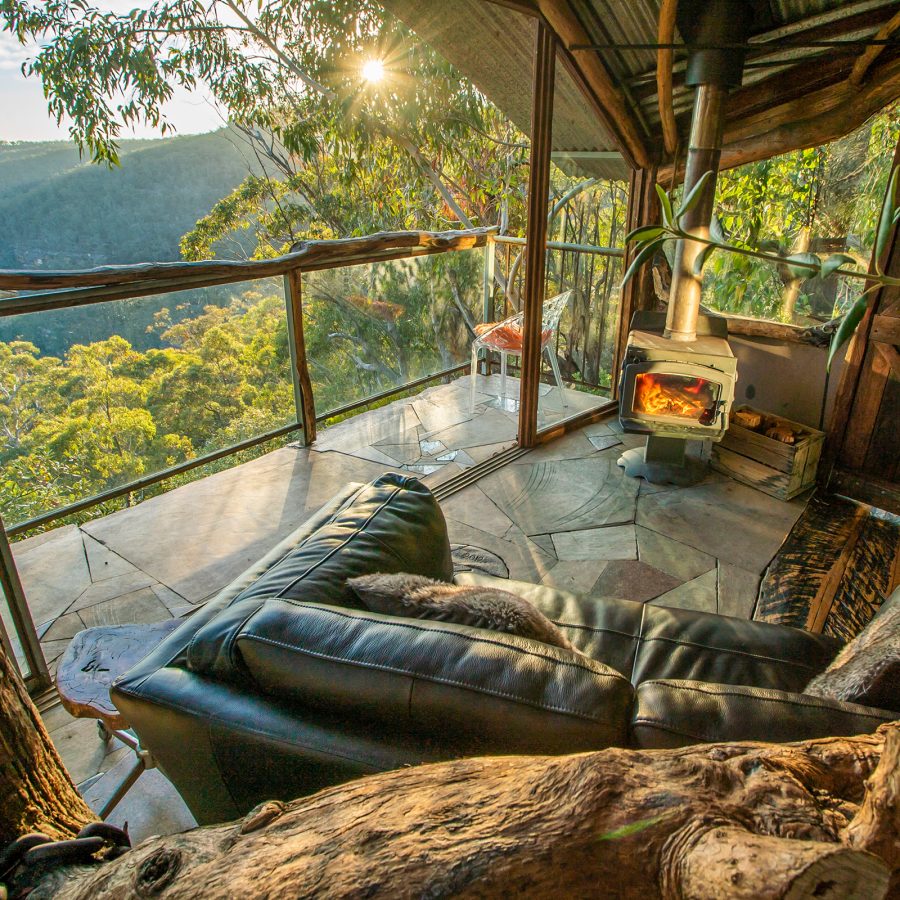 A living room with a sofa at The Secret Treehouse, Love Cabins, Blue Mountains. There is a balcony with a view of the mountains. 