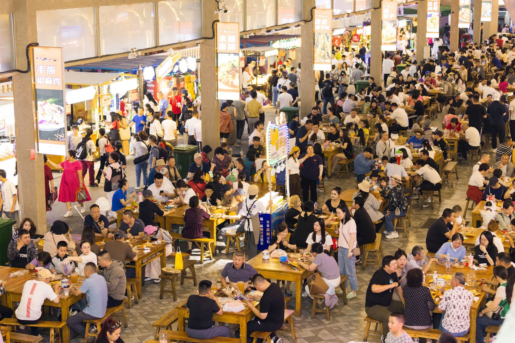 Many groups of people at tables in the crowded Xinjiang International Grand Bazaar.