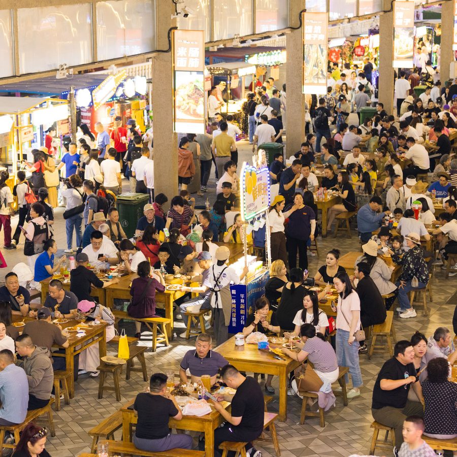 Many groups of people at tables in the crowded Xinjiang International Grand Bazaar.