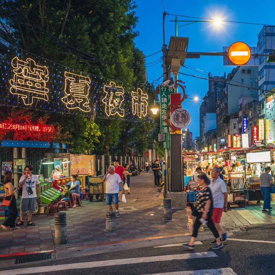Visitors walk around the perimeter of Ningxia Night Market in Taipei, which is surrounded by brightly lit shop signs.