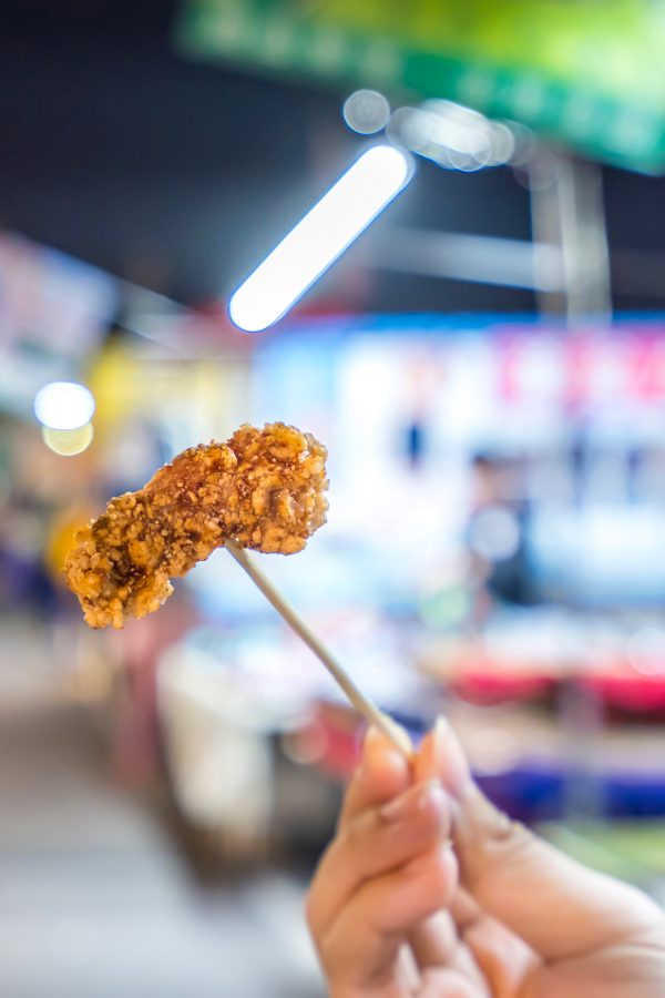 A visitor to the Nanjichang Night Market holds up a piece of fried chicken on a skewer.