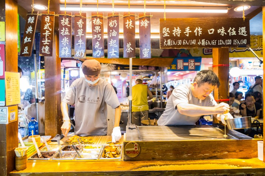 Two vendors work a food stall selling dorayaki, a Japanese pancake sandwich stuffed with red bean paste, at Raohe Night Market. 