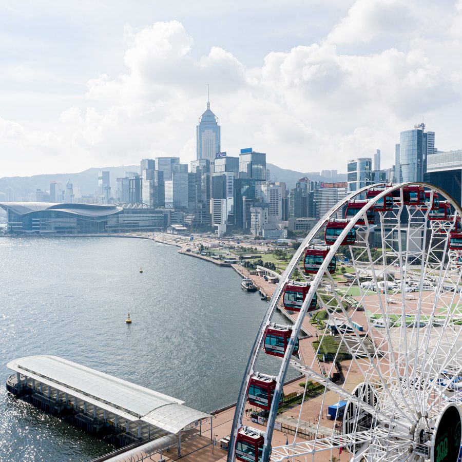 A bird’s eye view of the AIA Observation Wheel at the Central Harbourfront during daytime with a view of Victoria Harbour and iconic skyscrapers in Hong Kong.