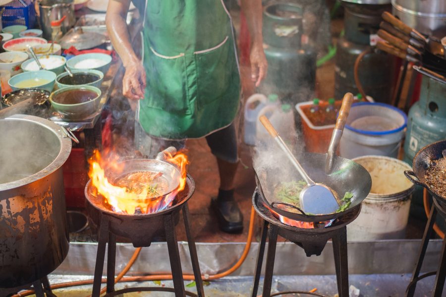 A person in an apron cooking food on stoves outdoors. 
