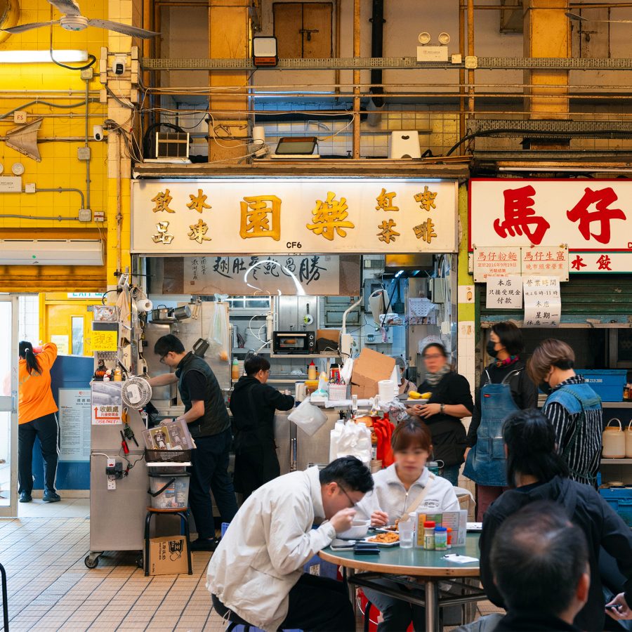 The storefronts of Lok Yuen and Ma Chai at Kowloon City Market and Cooked Food Centre. Staff are working in the restaurants while diners are eating at the tables. 