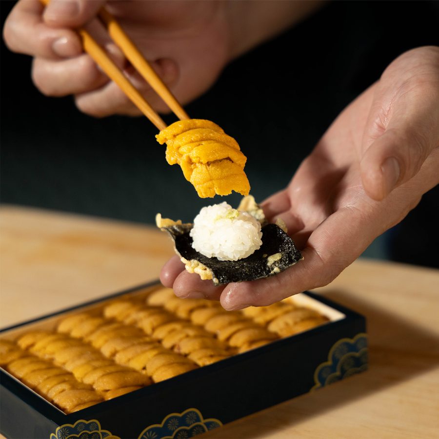 A person uses a pair of chopsticks to place a slice of fish on a small piece of rice.
