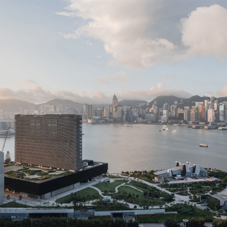 Aerial daytime view of M+ and Victoria Harbour with the skyline of Hong Kong Island in the background.