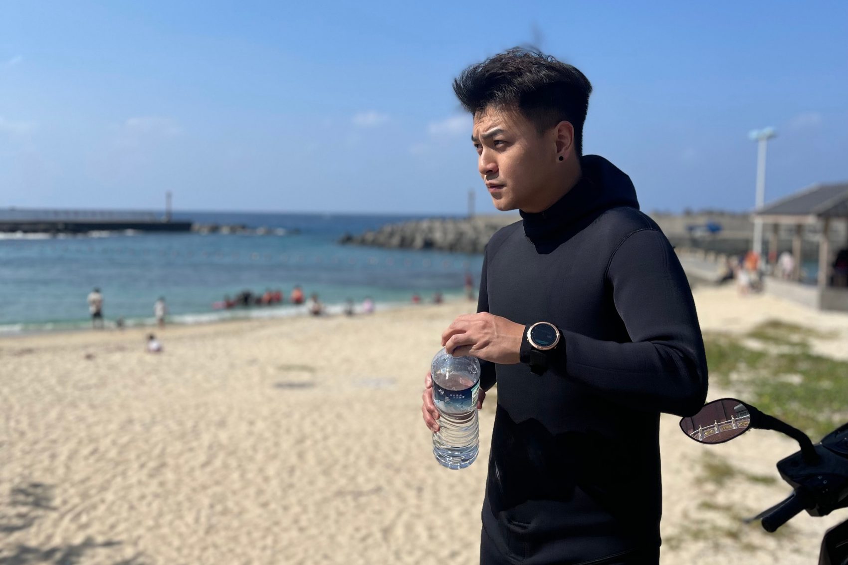 Cathay Pacific Flight Purser Don Yu stands on a sunny beach in Liuqiu; he is wearing a black wetsuit and holding a water bottle