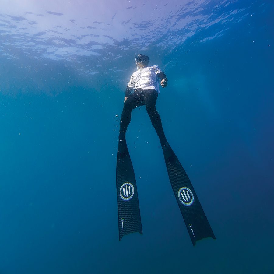 An underwater shot of Cathay Pacific Flight Purser Don Yu. Yu floats in the water, wearing a wetsuit and free diving fins