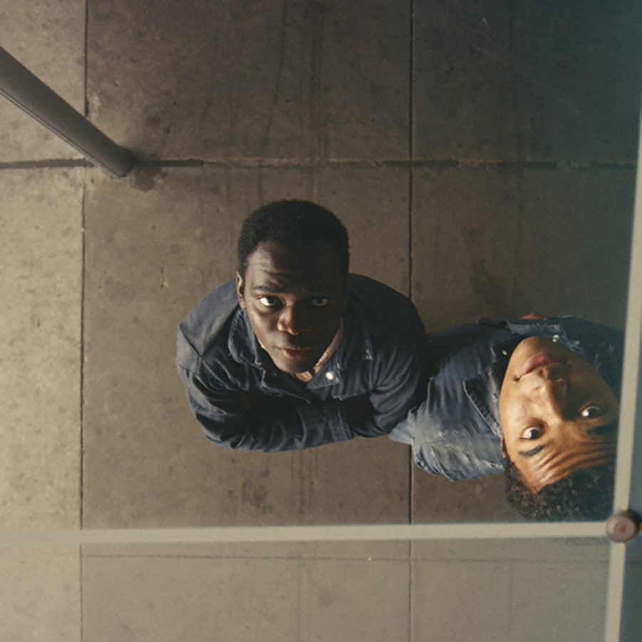 An aerial shot of teenage boys Elwood (Ethan Herisse) and Turner (Brandon Wilson) staring up through the pane of a glass roof in a scene from Nickel Boys. 