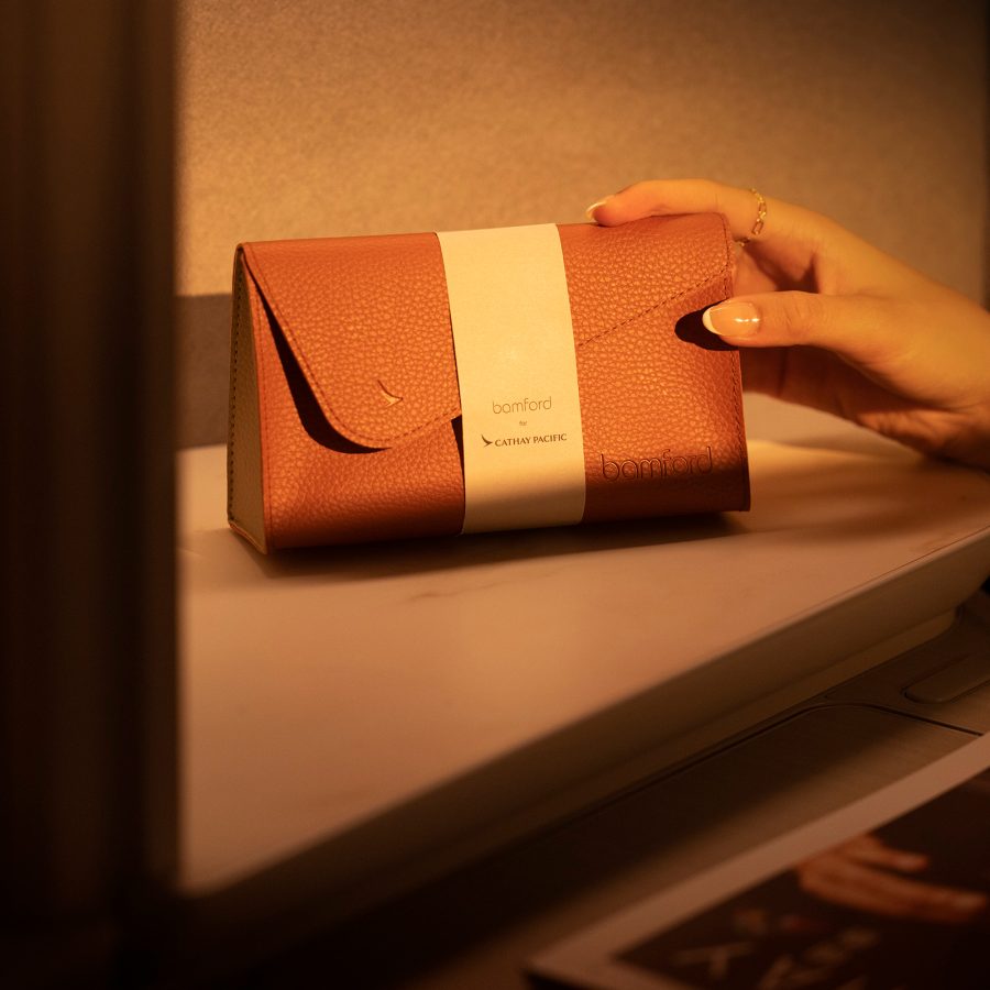 A hand holding the new Cathay Pacific Bamford amenity kit for women in brown colour inside the Aria suite of the Cathay Pacific business cabin.
