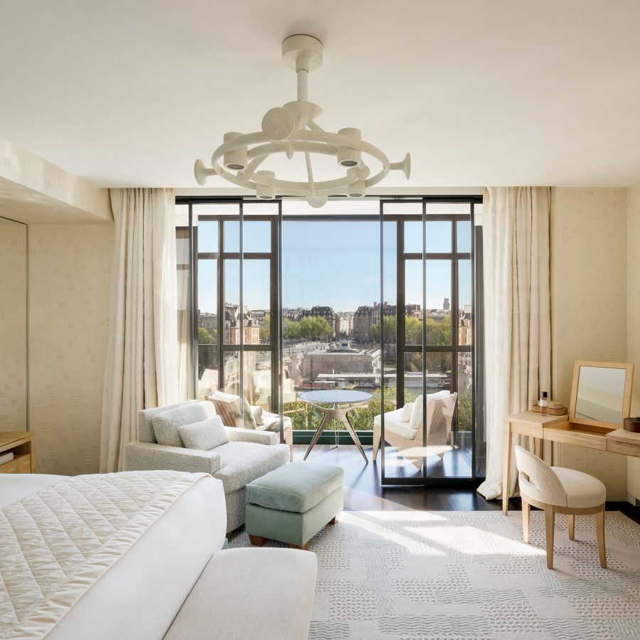 An interior view of a Cheval Blanc Paris bedroom suite with a balcony overlooking the city and lake during daytime.