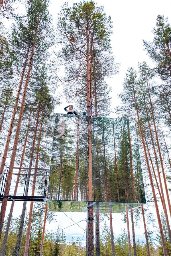 A view of the Mirrorcube capsule at Tree Hotel in Sweden, suspended between tall trees in a forest during daytime.