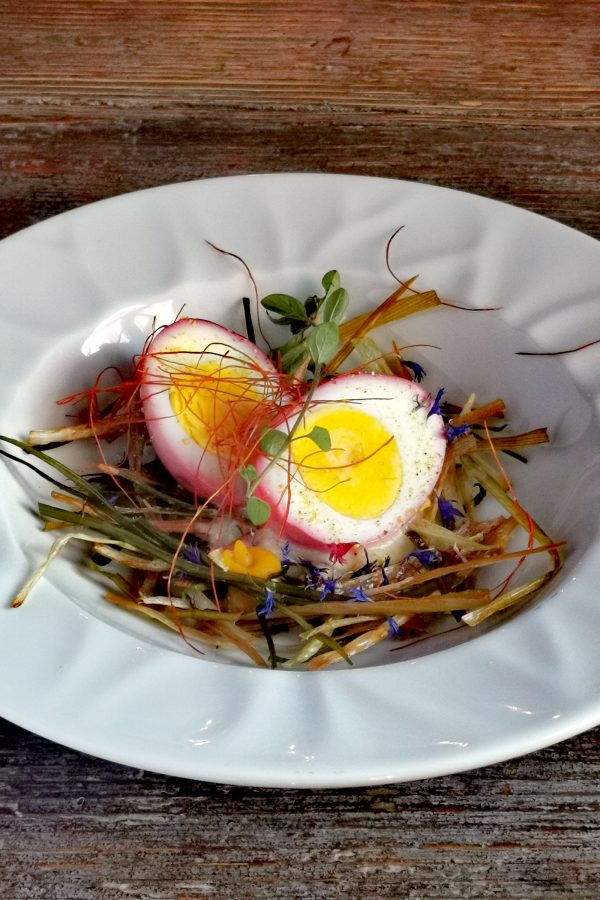  A closeup of a pink egg dish sitting on strands of vegetables in a white plate, served at Oasi di Galbusera Bianca in Curone Valley, Brianza near Milan. 