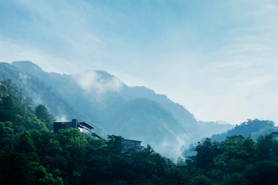 A landscape view of HOSHINOYA Guguan hotel in Taichung City, Taiwan, surrounded by lush greenery on a mountain, seen from a distance during daytime.