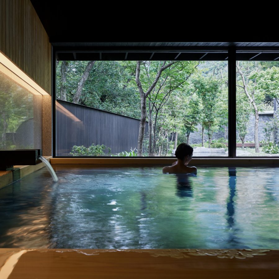 A view inside a hot spring bath with a calming view of trees outside the large windows at HOSHINOYA Guguan hotel in Taichung City, Taiwan.