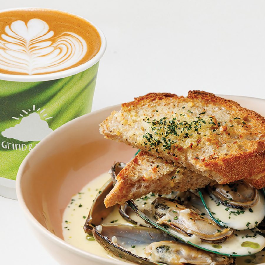 A closeup of a bowl of muscles in cream topped with toasted bread with a cup of latte, served at Grind & Brew at Airside mall in Hong Kong