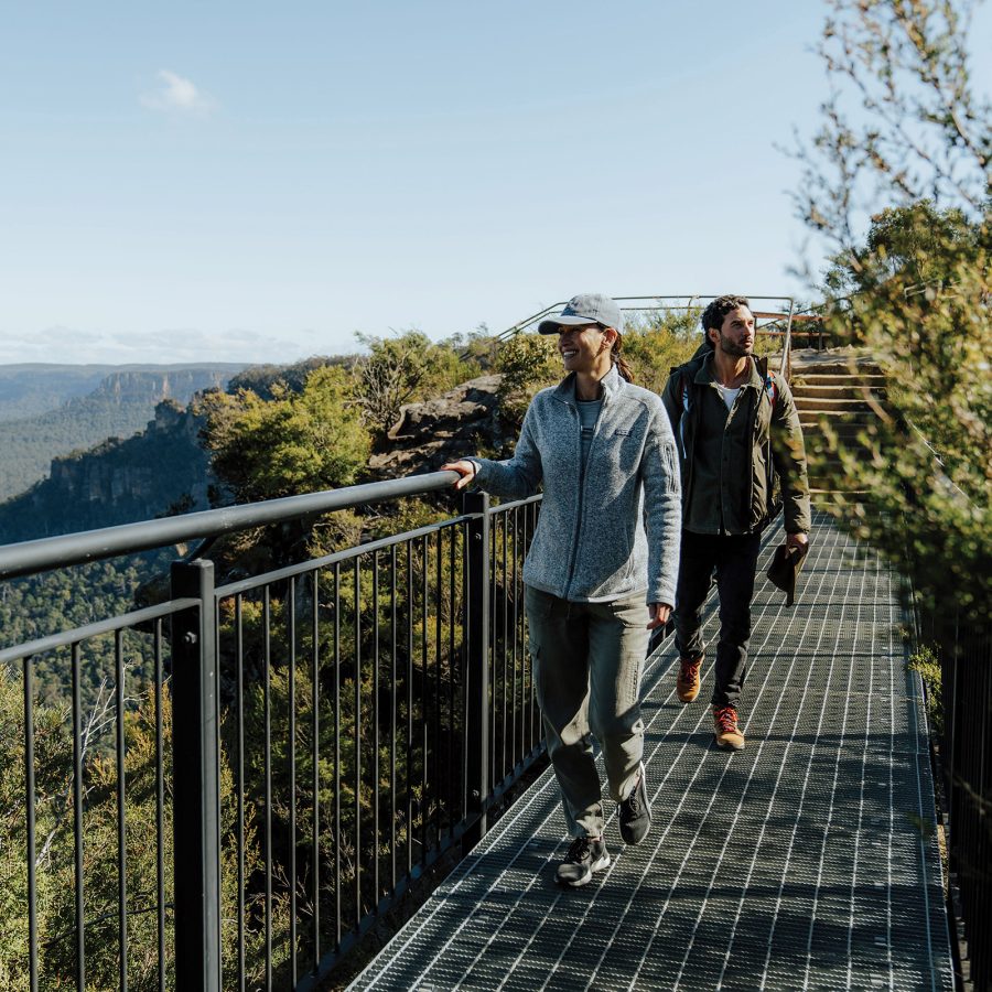 Two hikers crossing Buttonshaw Bridge while looking at the view along Grand Cliff Top Walk at the Blue Mountains National Park in Australia.