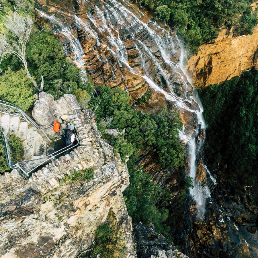 Two hikers admiring Katoomba Falls from above on Fletcher’s Lookout at the Blue Mountains National Park in Australia.