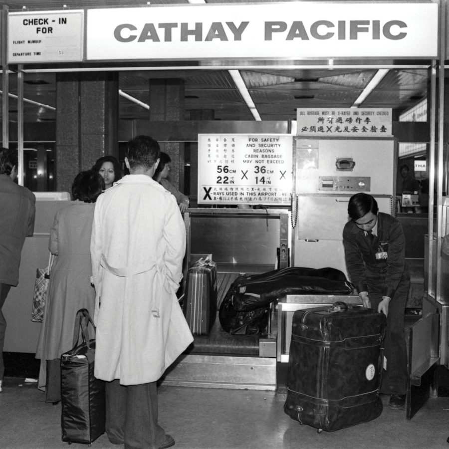 An old black-and-white image of Cathay Pacific airport crew handling luggage at a check-in counter the former old Kai Tak Airport in Hong Kong. 