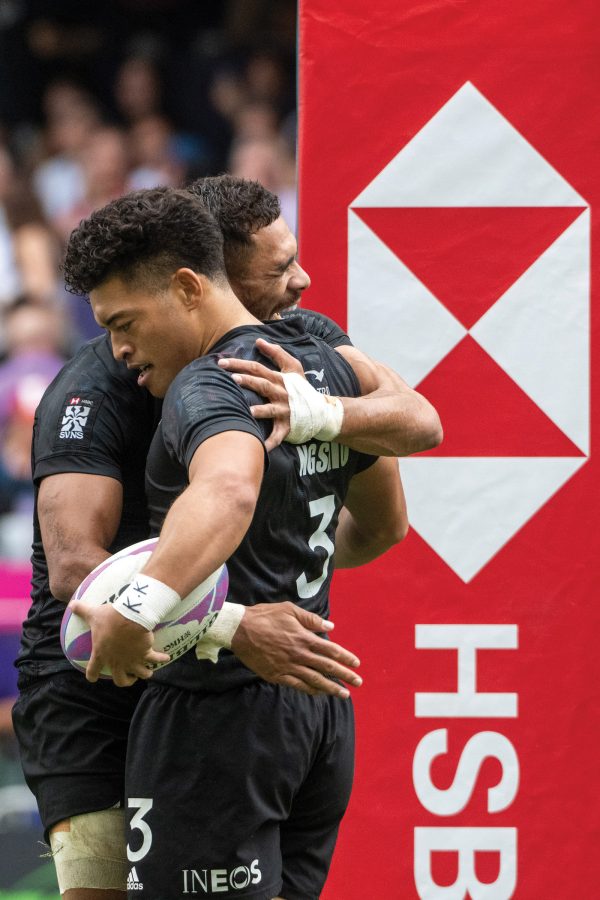 Two rugby players hugging on the field while holding a rugby ball.