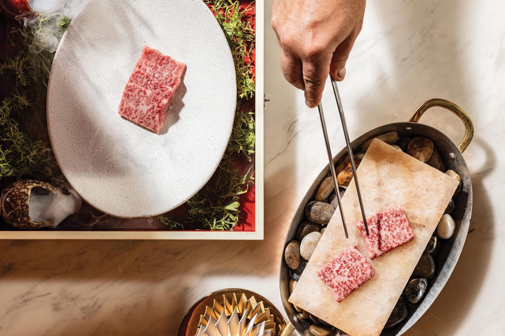 Chef holding out tongs as they handle slices of meat at Nuri Steakhouse