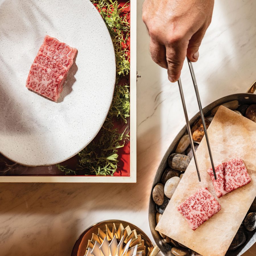Chef holding out tongs as they handle slices of meat at Nuri Steakhouse