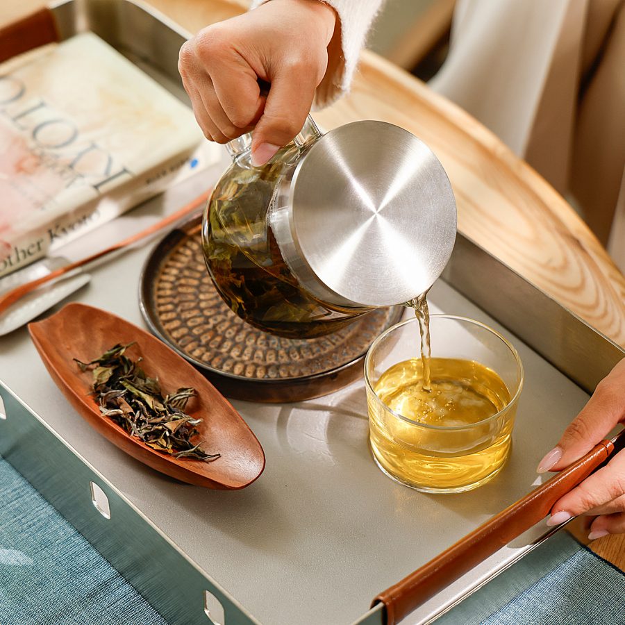 A person pours tea into a glass cup atop an upcycled tray, a new item in Cathay’s upcycled collection.