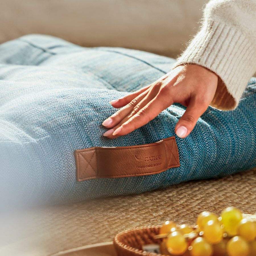 A person puts their hand on a green upcycled floor cushion from Cathay’s new collection.
