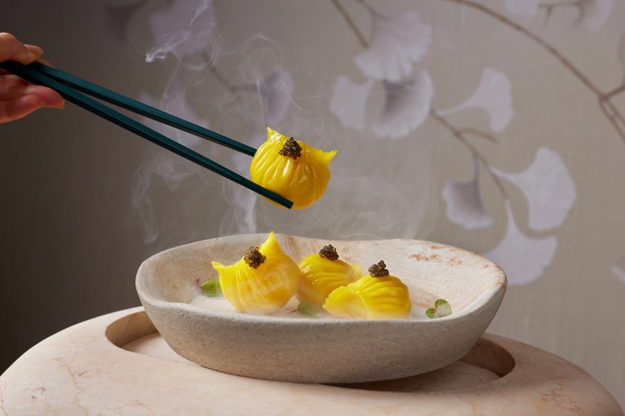 A hand holding chopsticks picks up a saffron-infused shrimp dumpling at Hoi King Heen, Hong Kong.