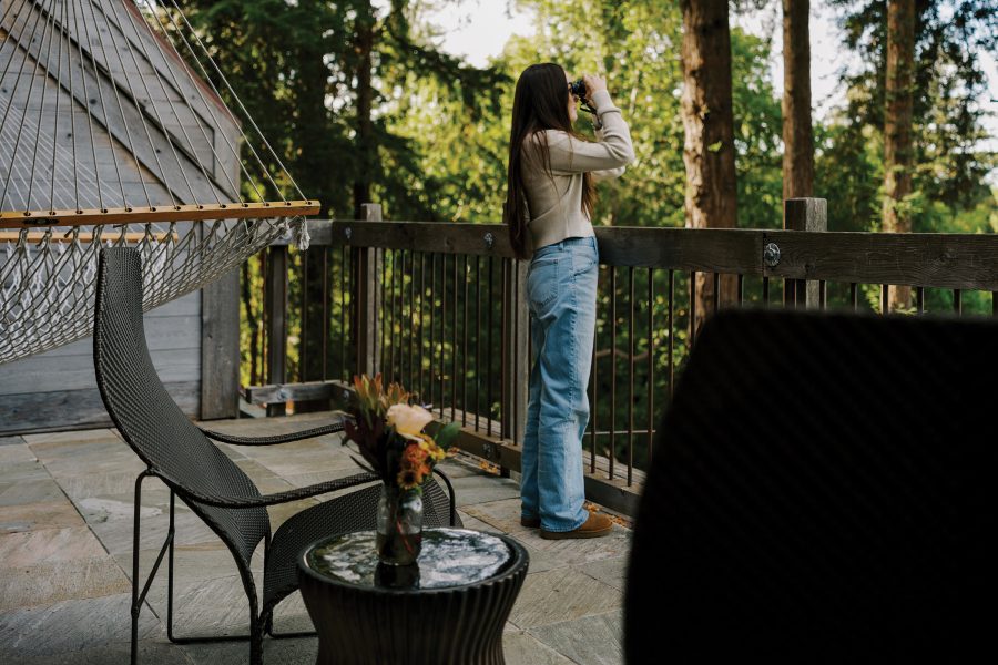 A woman looking into nature through a pair of binoculars on an outdoor terrace at Alila Ventana Big Sur, surrounded by trees