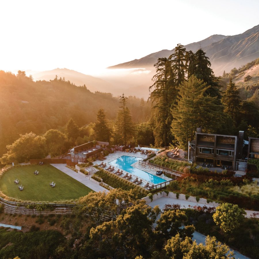 A bird’s eye view of the sun rising over the outdoor swimming pool and luxury resort at Alila Ventana Big Sur on a forrested hill, surrounded by nature