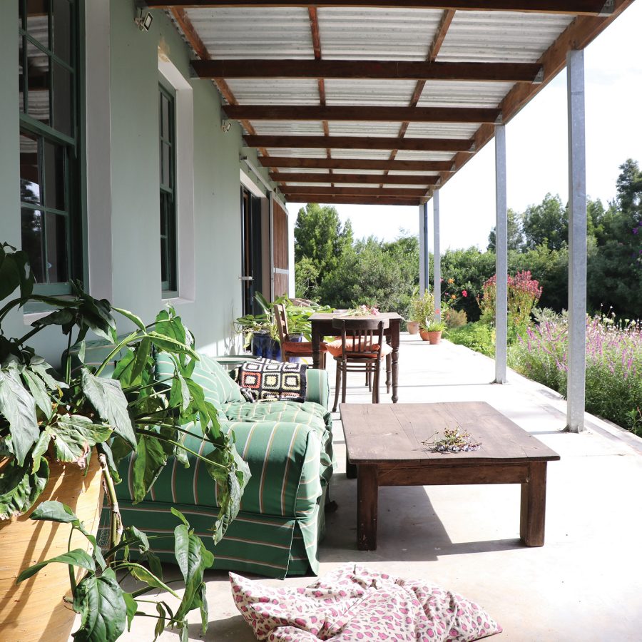An exterior view of the shaded porch at The School Farmstay in South Africa surrounded by flowers and greenery
