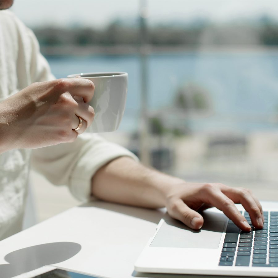 A man holding a cup and working on a laptop by the window with a view of the airport runway at a Cathay Pacific lounge.