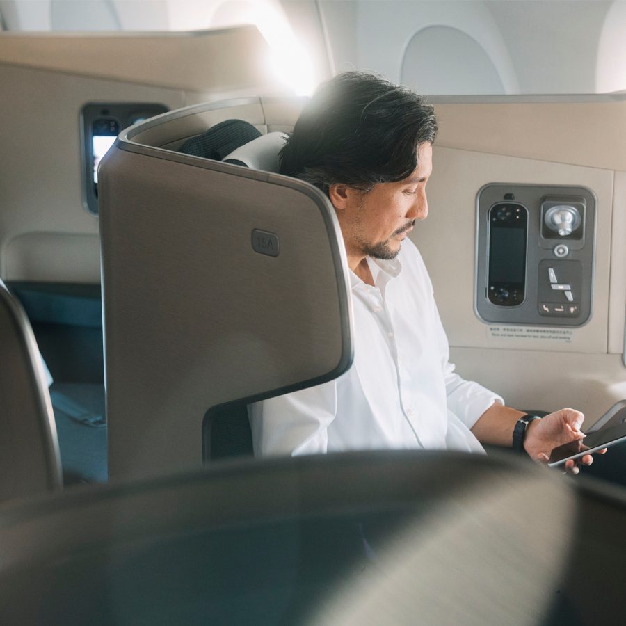 A man using a smartphone while sitting in Cathay Pacific’s Aria Suite First class cabin.