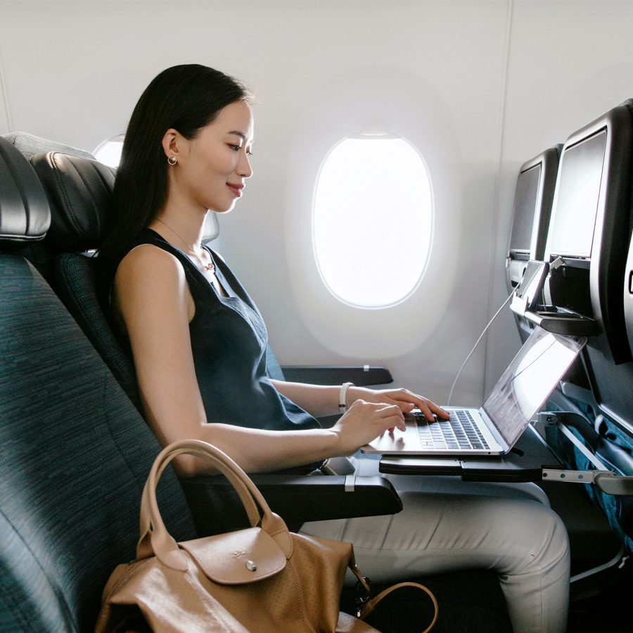 A woman sitting by the window and working on a laptop in a Cathay Pacific aircraft with a handbag on the next seat.