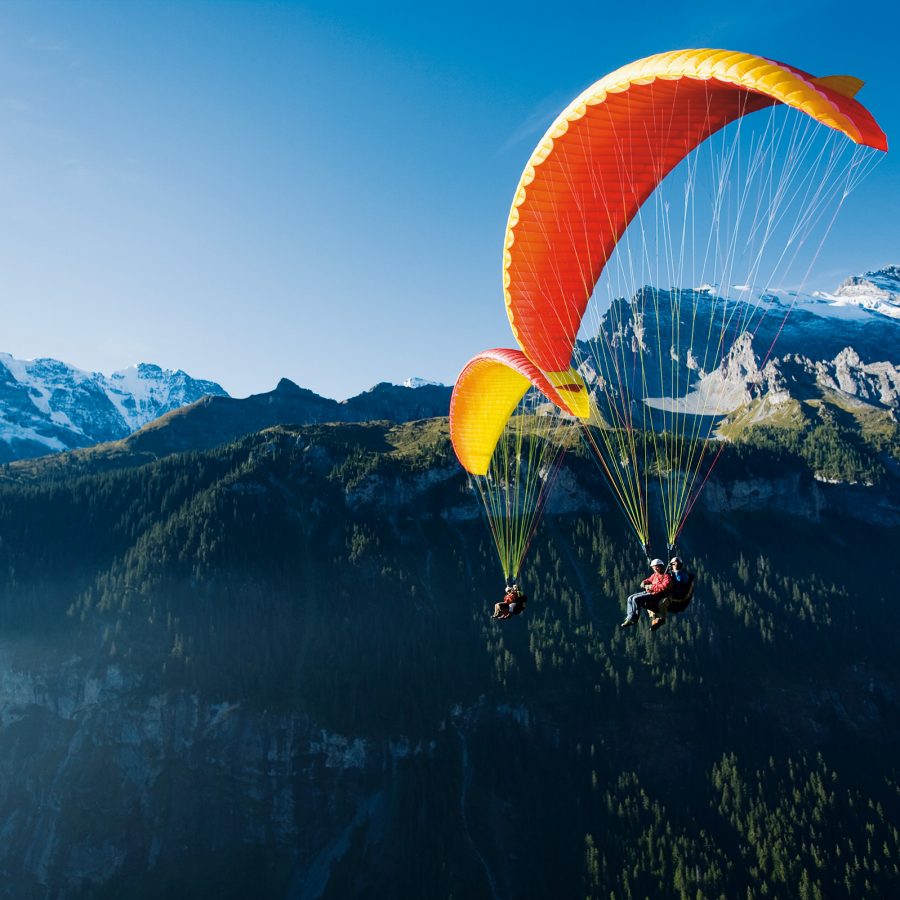 Two paragliders in the air with a view of the Swiss mountain range in the backdrop.