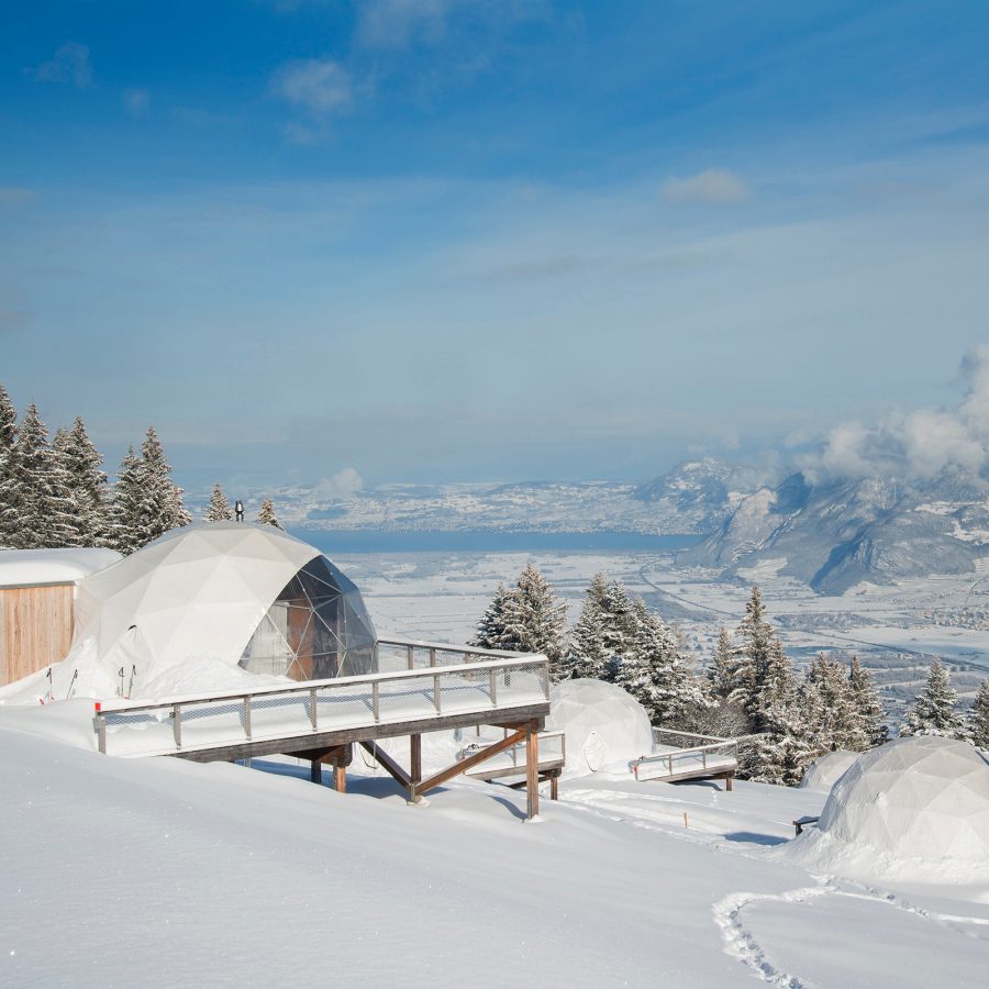 An exterior view of snow-capped Whitepod geodesic dome tents during a clear day in Switzerland.