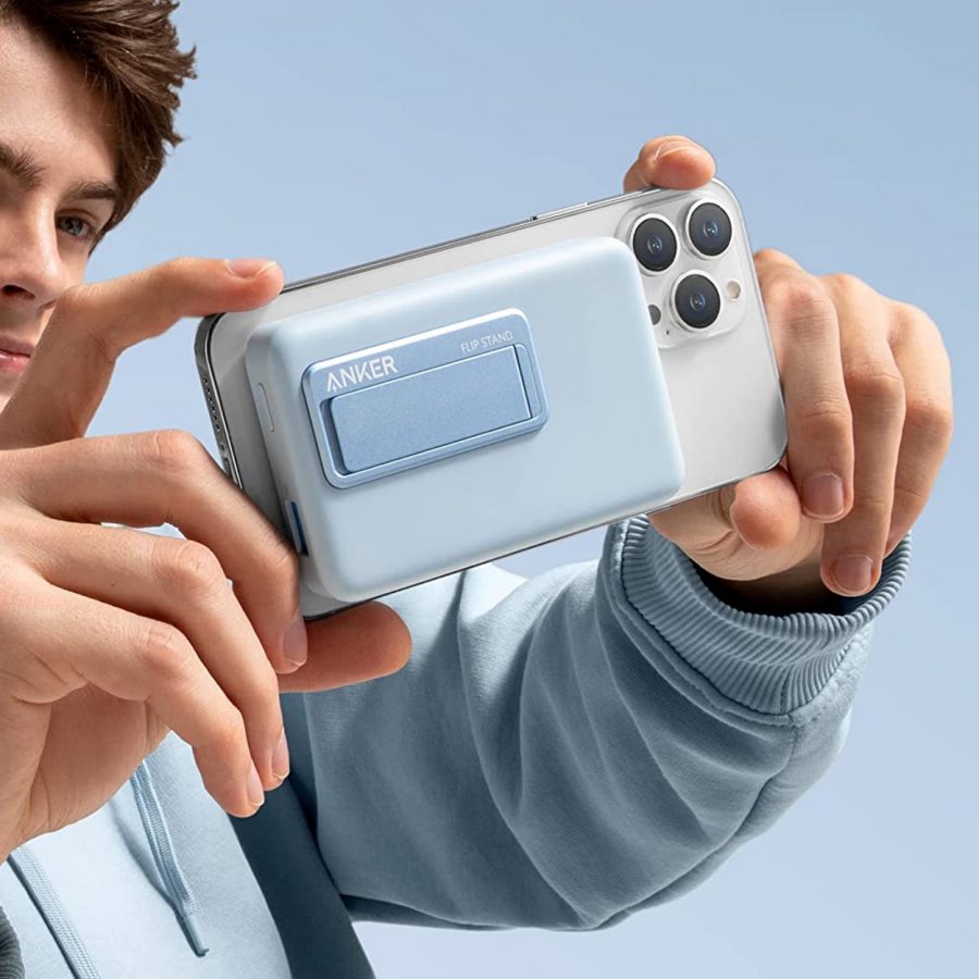 A man holding a phone with a blue Anker portable charger attached to it.