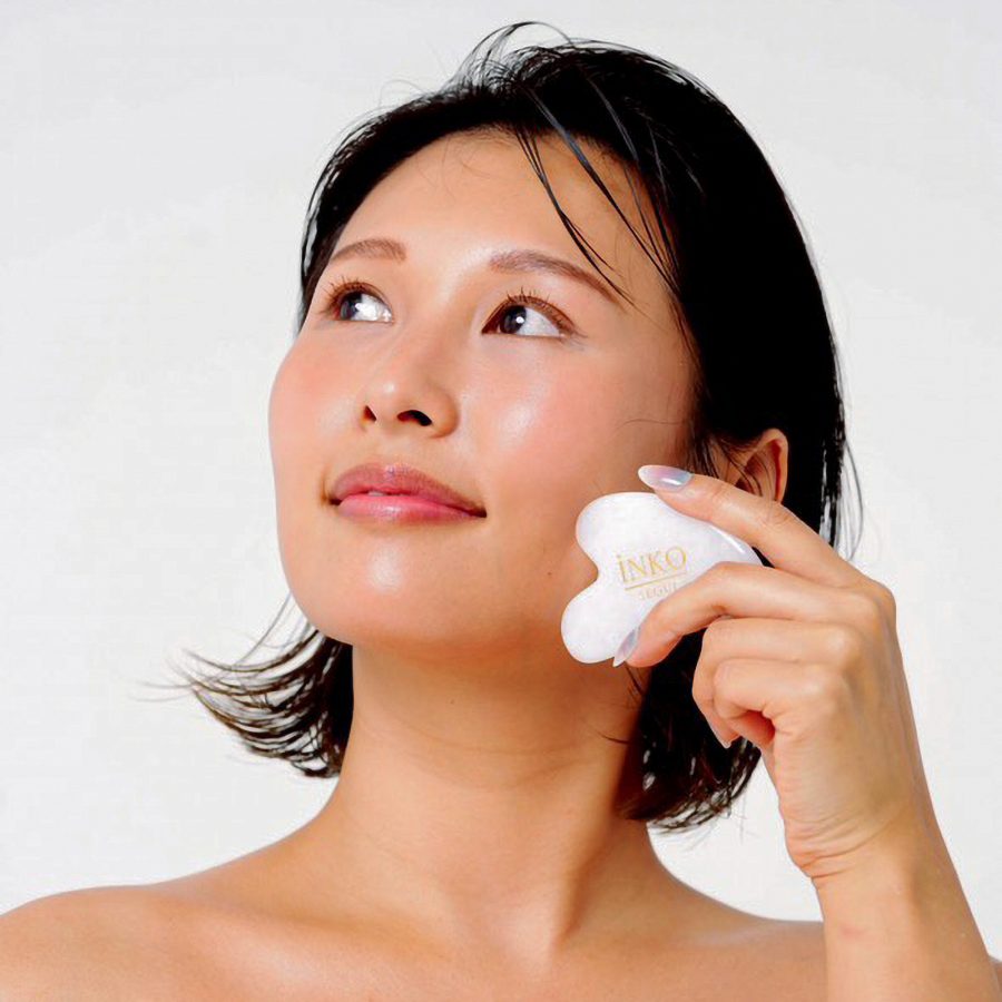 A  woman holding a gua sha instrument to her face. 