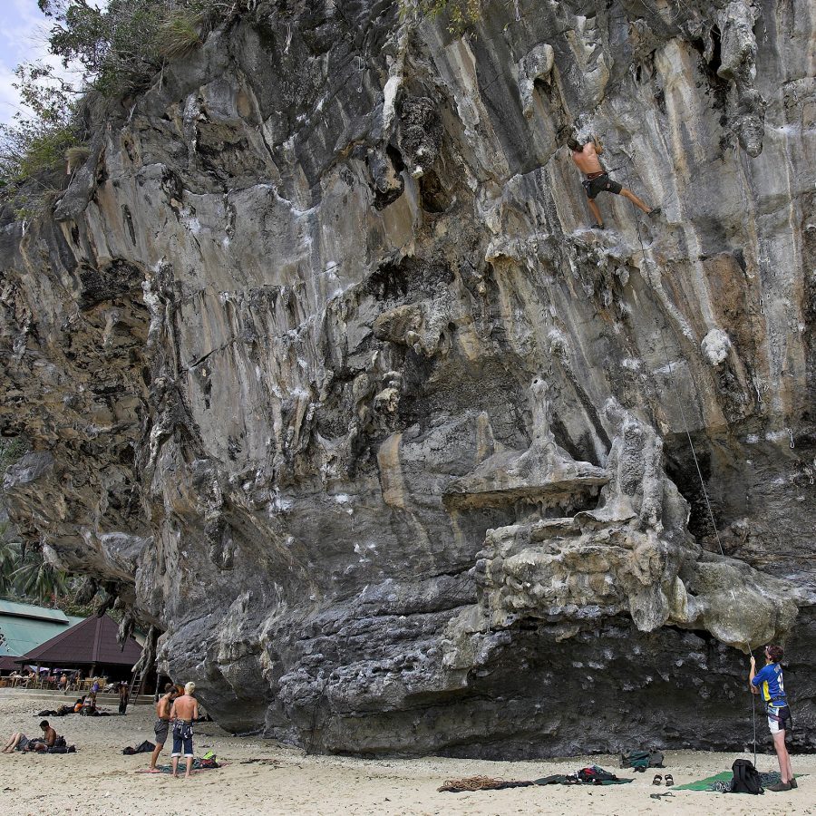 A view of Railay Beach Dragonite East in Krabi, Thailand, seen from inside a cave with lush green foliage on a sunny day.
