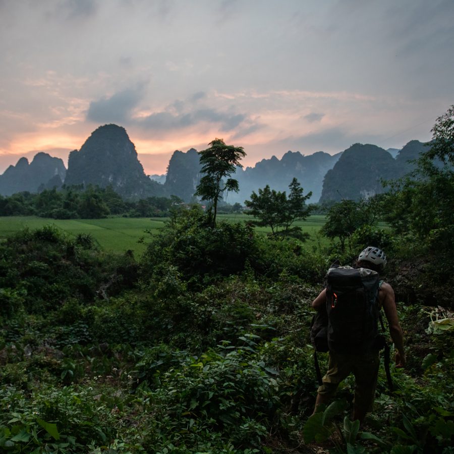 A silhouette of a person walking amidst greenery at Huu Lung climbing cliff at sunset.