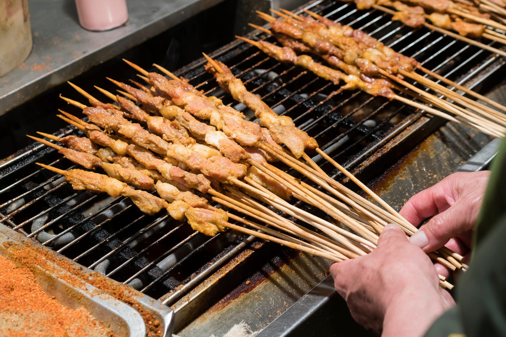 A closeup of a street food vendor in Beijing cooking skewers of shish kebabs over a grill.