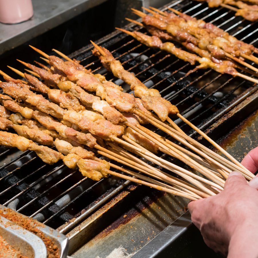 A closeup of a street food vendor in Beijing cooking skewers of shish kebabs over a grill.
