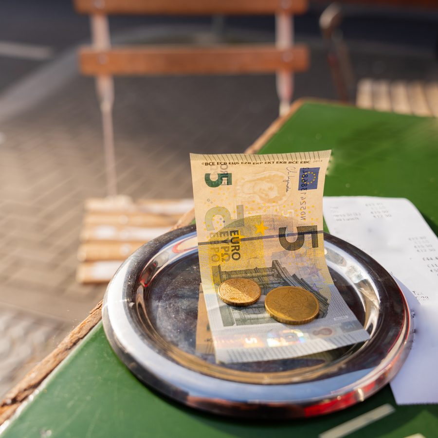 Close up on a 5 Euro note on a small silver plate with a bill next to it on a table. 