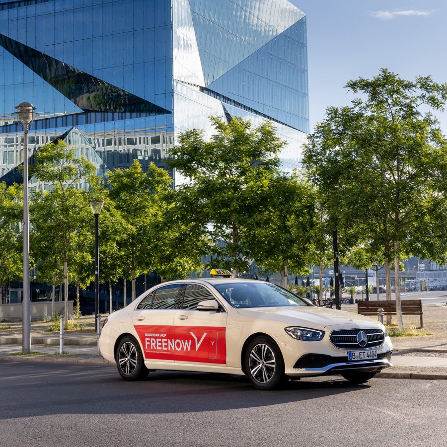 Shot of a white taxi in Munich with the Free Now app logo on the side.